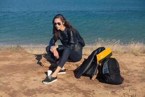 Travel concept. Young woman with sunglasses and backpack sitting resting with sea view. photo