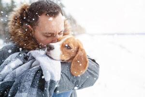 A young man wrapped his best friend Beagle dog in a warm blanket to warm him in a cold snowy winter. photo