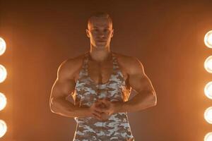 Active lifestyle. Professional bodybuilder showing biceps and smiling at camera, lamps illumination on background photo