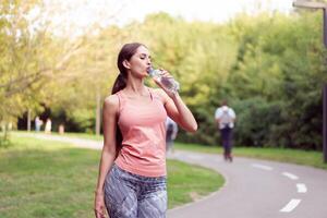 Athletic woman standing running track in summer park drink water after running exercises photo