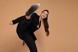 Businesswoman hitting with leg in camera dressed black office suit smile isolated on color background. Fight for business. Martial Art Karate pose in the studio on grey background. Kung fu style photo