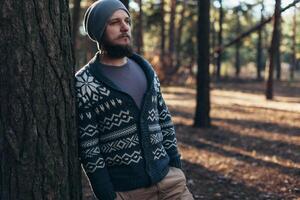 un joven hombre con un barba camina en un pino bosque. retrato de un brutal barbado hombre otoño bosque foto