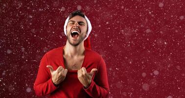 Young handsome caucasian guy in red sweater and Santa hats stands on red background in studio  Shows how hot he is photo