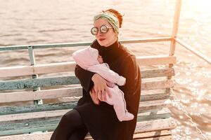 joven madre que lleva su adorable bebé hija en un bebé portador en hermosa otoño parque detrás el lago foto