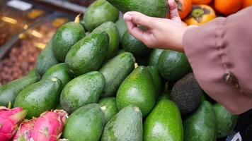 young woman hand choosing avocado at fruits market video