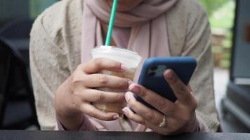 vrouw hand- Holding slim telefoon en drinken verkoudheid koffie video