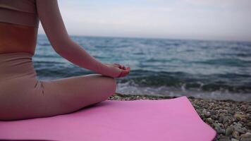 jong vrouw met zwart haar, geschiktheid instructeur in leggings en tops aan het doen uitrekken en pilates Aan yoga mat in de buurt de zee. vrouw geschiktheid yoga routine- concept gezond levensstijl harmonie en meditatie video