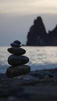 equilibrato roccia piramide su mare ciottoli spiaggia, chiaro cielo a tramonto. d'oro mare bokeh su sfondo. verticale video, zen pietre su mare spiaggia, meditazione, terme, armonia, calma, equilibrio concetto. lento movimento video