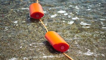 Orange safety buoys on a rope floating in the sea on a sunny day, close up. Fencing of the swimming area on the beach. video