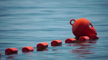 Orange safety buoys on a rope floating in the sea on a sunny day, close up. Fencing of the swimming area on the beach. video