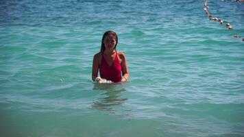 jung Frau mit lange Haar im ein rot Badeanzug und Armbänder im Boho Stil genießen das Wellen auf das Strand im Sommer. bezaubernd glücklich feminin entspannend beim Sommer- Strand haben Urlaub. schleppend Bewegung. video