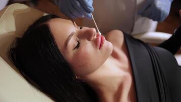 Cosmetologist is applying cream with anesthesia on patient lips skin before augmentation procedure. Woman in beauty clinic with doctor beautician preparing to treatment using numbing cream video