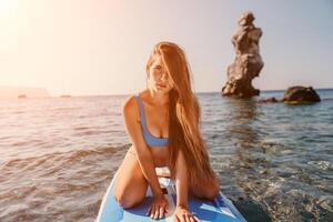 Woman sea sup. Close up portrait of happy young caucasian woman with long hair looking at camera and smiling. Cute woman portrait in a blue bikini posing on sup board in the sea photo