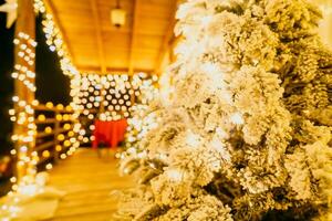 cubierto de nieve Navidad árbol con brillante blanco luces situado al aire libre cerca un edificio, un acogedor festivo momento. foto