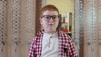 Red-haired Caucasian boy in a checkered red and white shirt puts on glasses looking straight into the camera video