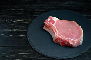 Top view of one pieces raw pork chop steaks on a black stone cutting board. photo