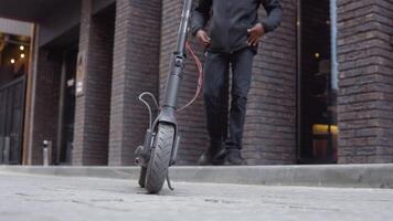 ung afrikansk amerikan i svart Tröja och svart jeans på de bakgrund. ett elektrisk skoter är i de förgrund video