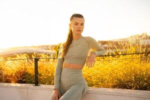 Sportswoman sitting on fence in summer park after morning workout photo