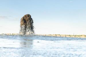 A large fountain of water mixed with sand that beats from a metal pipe against a blue sky. Sand mining. photo