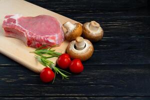 Top view of one pieces raw pork chop steaks with cherry tomatoes rosemary Champignon mushrooms and garlic on a cutting board. photo