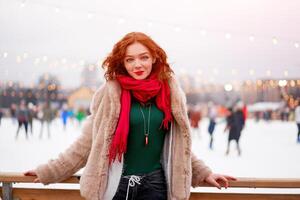 Young beautiful redhead girl freckles ice rink on background. Pretty woman curly hair portrait walking on new year fair photo