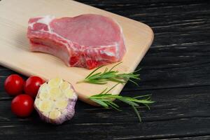 Top view of one pieces raw pork chop steaks with cherry tomatoes rosemary and garlic on a cutting board. photo