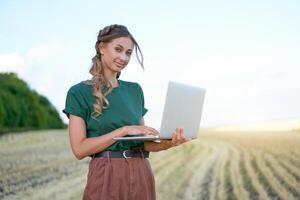 Woman farmer smart farming standing farmland smiling using laptop Female agronomist specialist research monitoring analysis data agribusiness photo