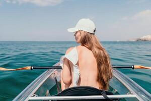 Woman in kayak back view. Happy young woman with long hair floating in transparent kayak on the crystal clear sea. Summer holiday vacation and cheerful female people relaxing having fun on the boat photo