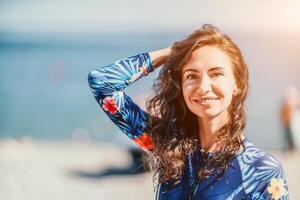 Portrait woman sea. Well looking middle aged smiling woman with black hair, fitness instructor in blue swimwear on the rocky beach near the sea. Female fitness yoga routine concept. Healthy lifestyle. photo