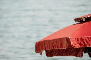 Red Beach Umbrella on the Background of the Blue Sea Ocean. Beach Landscape. Summer travel and holidays concept. photo