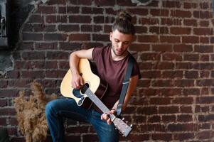 Man with acoustic guitar against brick wall playing music singing songs enjoy life Medium shoot photo