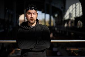 Handsome young unshaven man black hoodie and bandana stands photo