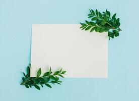 Desktop mock-up with blank paper card, branch on white shabby table background. Empty space. Styled stock photo, web banner. Flat lay photo