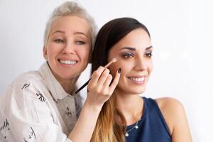 Make-up artist applying bright base color eyeshadow on model's eye and holding a shell with eyeshadow on background photo