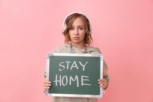 Stay home concept Woman with headphones dressed oversize hoodie holds chalkboard with the words stay home photo