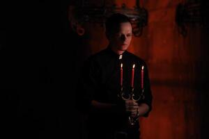 Portrait of handsome catholic priest or pastor with dog collar, dark red background. with three red candle in the hand photo