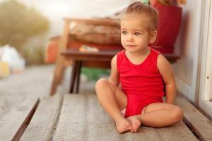 A boy sitting in the threshold of the house outside and smiling. He is wearing a red shirt. summer day. Horizontal. photo