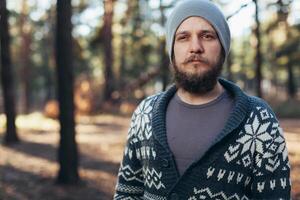 un joven hombre con un barba camina en un pino bosque. retrato de un brutal barbado hombre otoño bosque foto