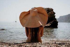 Woman travel sea. Happy tourist in hat enjoy taking picture outdoors for memories. Woman traveler posing on the beach at sea surrounded by volcanic mountains, sharing travel adventure journey photo