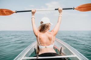 Woman in kayak back view. Happy young woman with long hair floating in transparent kayak on the crystal clear sea. Summer holiday vacation and cheerful female people relaxing having fun on the boat photo