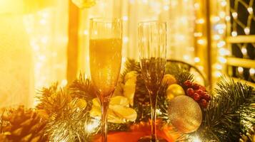 Two champagne glasses filled with champagne are placed on a table with a fruit arrangement. The glasses are surrounded by lights, creating a festive atmosphere. photo