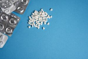 Empty used blisters from tablets silver and white color and pills lie on blue medical background photo