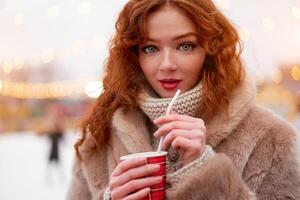 Young beautiful redhead girl freckles ice rink on background. Pretty woman curly hair portrait walking on new year fair photo