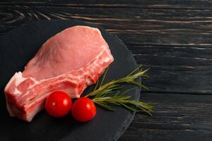 Top view of one pieces raw pork chop steaks with cherry tomatoes on a black stone cutting board. photo