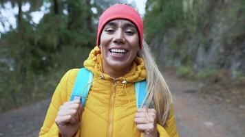 uma mulher dentro uma amarelo Jaqueta e vermelho chapéu sorrisos enquanto caminhando em uma trilha video