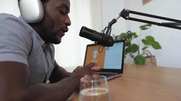 uma homem dentro fones de ouvido senta às uma mesa com uma computador portátil e uma vidro do água video