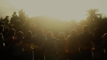 uma grupo do pessoas a partir de diferente geração estão em pé juntos dentro pôr do sol video