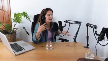 un mujer haciendo podcast vistiendo auriculares y un auriculares es sentado a un escritorio con un computadora pantalla video