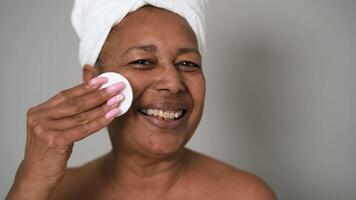 uma mulher com uma toalha em dela cabeça é sorridente enquanto usando uma facial limpeza almofada video