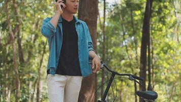 A man pushes a bicycle and walks happily to relax in the park after cycling for exercise. video